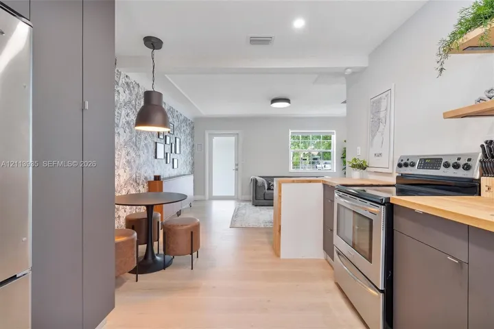 Kitchen featuring flat-panel cabinetry, stainless steel appliances, wood-finish countertops, decorative wall covering, and recessed lighting