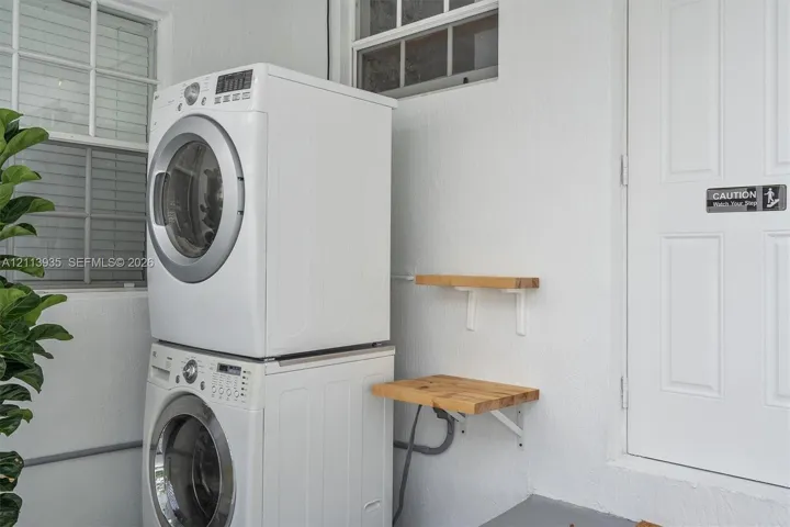 Stackable front-loading washer and dryer, mounted wood-finish shelving, and multi-pane windows