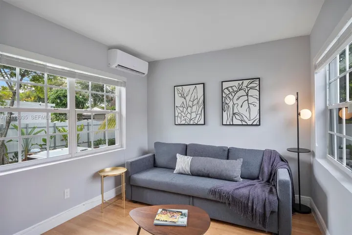 Room featuring light-toned wood-finish flooring, white walls, grid-pattern windows, and a wall-mounted ductless climate control unit