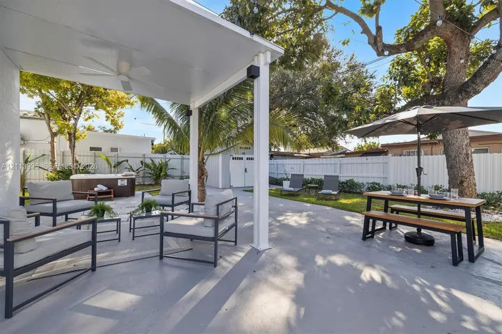 Covered patio featuring a ceiling fan, concrete flooring, exterior-grade hot tub, white vinyl fencing, and a detached structure