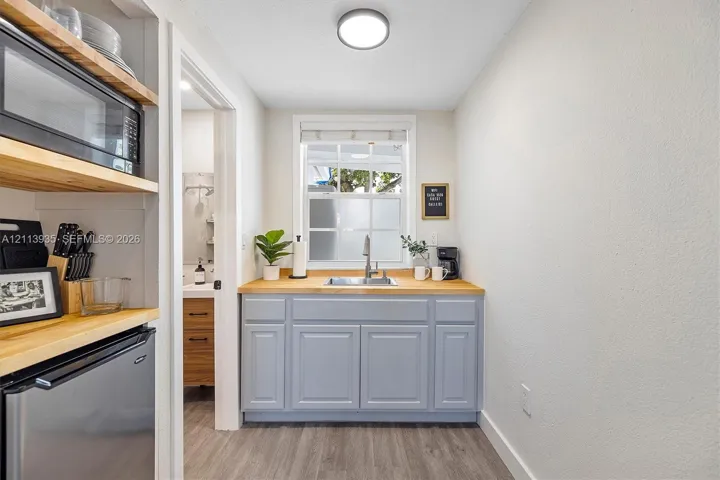 Wet bar featuring light-toned wood-finish countertops, grey shaker-style cabinetry, a drop-in stainless steel sink, and wood-finish flooring