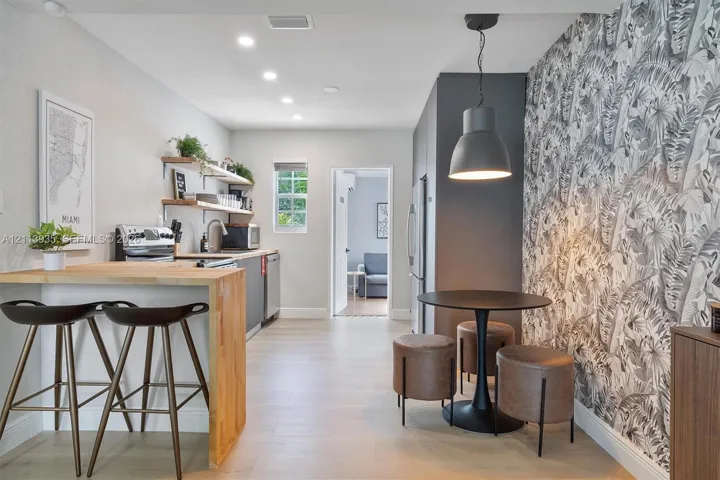 Kitchen featuring wood-finish flooring, breakfast bar with butcher block countertop, recessed lighting, patterned accent wall, and matte black pendant lighting