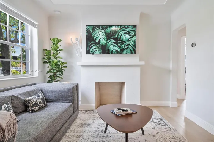Living space featuring a central fireplace with a crisp white mantel, wood-finish flooring, and a multi-pane window