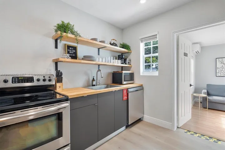 Kitchen featuring charcoal-toned cabinetry, wood-surface countertops, stainless steel appliances, and mounted wood shelving