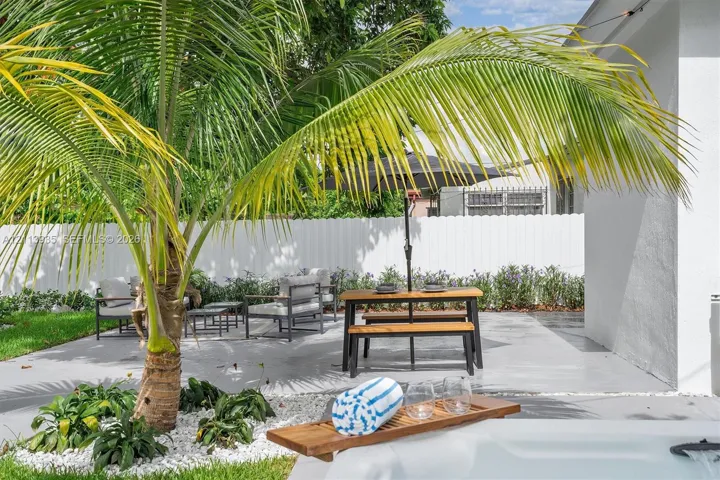 Private outdoor area featuring a concrete patio, white vinyl privacy fencing, landscaped garden beds with decorative stone, and a mature palm tree