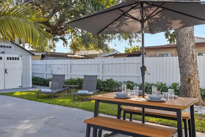 Backyard featuring a paved patio, white privacy fencing, manicured lawn, and a detached storage structure