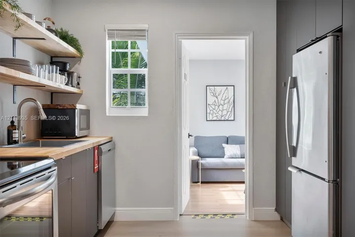 Kitchen featuring wood-finish countertops, open wood shelving, dark cabinetry, stainless steel appliances, and a window with muntin detailing
