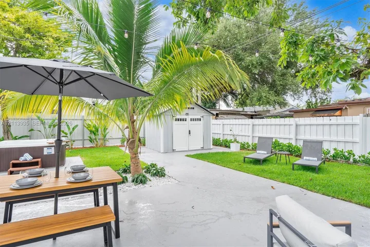 Backyard featuring a concrete patio, white vinyl fencing, mature landscaping, and a detached storage structure