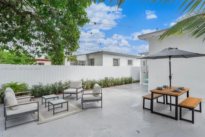 Outdoor patio featuring smooth concrete flooring, a full-height perimeter privacy fence, integrated overhead string lighting, and mature canopy trees