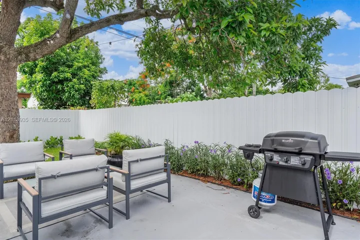 Concrete patio area featuring a white privacy fence, mature shade tree, and established perimeter landscaping