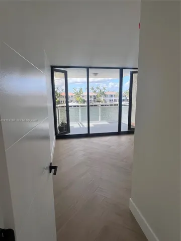 Herringbone-patterned wood-finish flooring, floor-to-ceiling glass panel doors, and a waterfront balcony with a railing