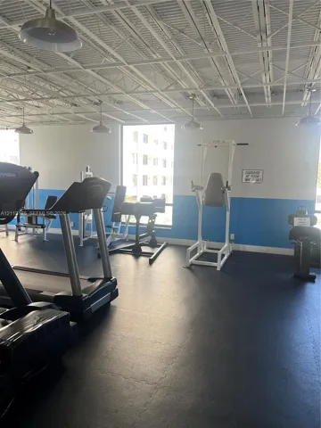 Fitness space featuring rubberized flooring, exposed industrial ceiling, and pendant lighting