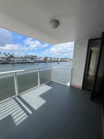 Covered balcony featuring water frontage, white metal railing, solid flooring, and textured wall finish
