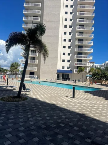 High-rise building featuring stacked private balconies, an outdoor swimming pool, and stone-paver decking