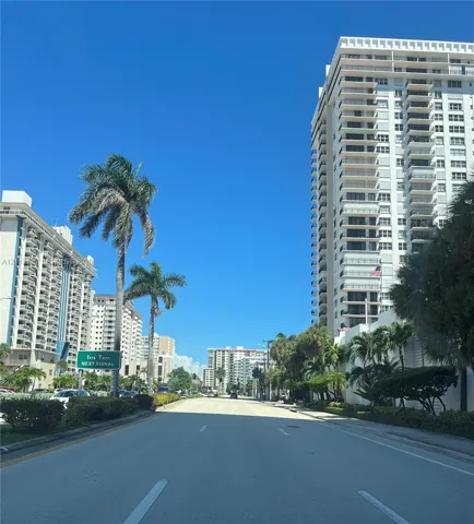 High-rise residential buildings featuring multi-level private balconies, exterior concrete structural elements, and established palm tree landscaping