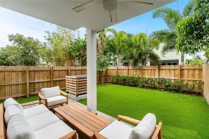 Covered patio featuring a ceiling fan, wood-style fencing, synthetic turf lawn, and exterior privacy landscaping