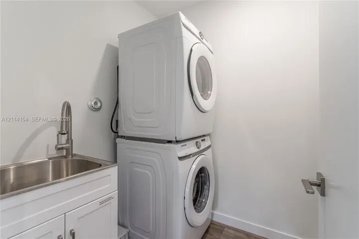 Stacked front-load laundry units with a white finish, stainless steel basin sink, and high-arc brushed nickel faucet set within a white cabinet vanity