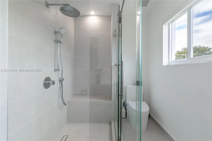 Walk-in shower with light-toned tiled surround, built-in tiled bench, rainfall shower head, adjustable handheld sprayer, and frameless glass enclosure