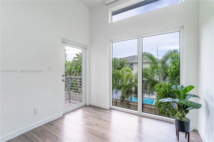 High ceilings featuring expansive picture windows and clerestory glass, wood-finish flooring, and a glass-panel exterior door opening to a balcony