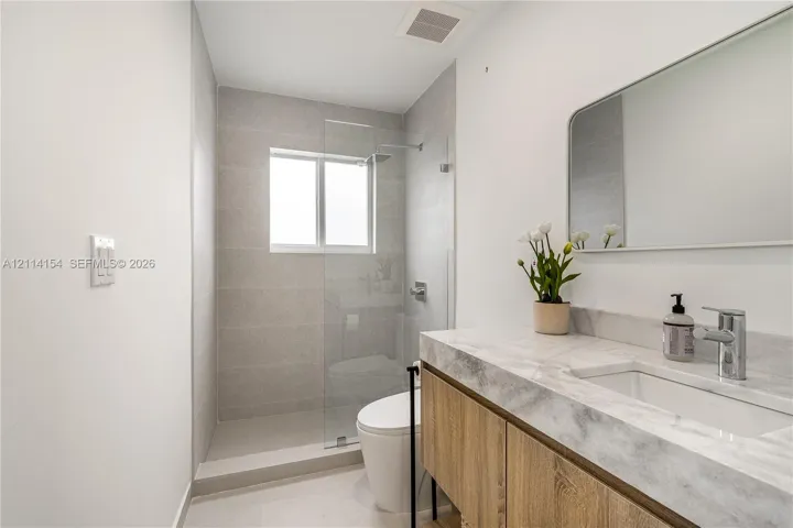 Bathroom featuring a floating wood-finish vanity, stone-topped integrated sink, glass-enclosed shower with full-height tile surround, and a wall-mounted rectangular mirror