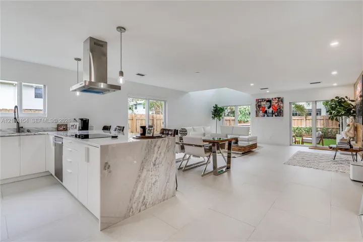 Kitchen featuring white cabinetry, stone-surface waterfall island, stainless steel range hood, and large-format tile flooring