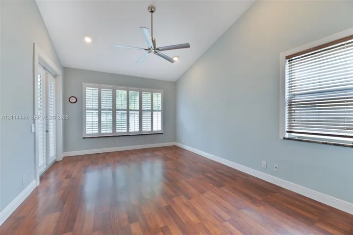 Vaulted ceiling, wood-finish flooring, multi-pane window with plantation shutters, recessed lighting, and dual glass-pane doors