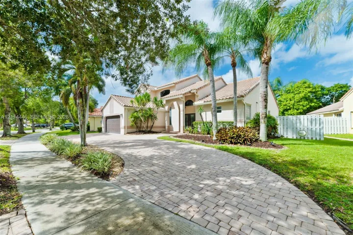 Stucco exterior featuring a tile roof, arched entryway, brick-paver driveway, and mature palm landscaping