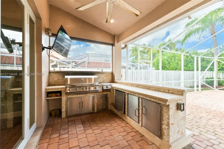 Covered outdoor kitchen featuring a built-in stainless steel grill, stone-finish countertops, stainless steel cabinetry, and brick paver flooring within a screened-in lanai