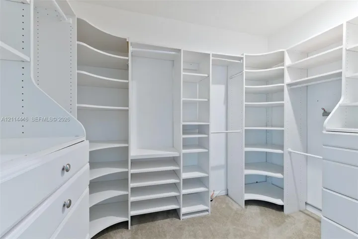 Walk-in closet featuring white built-in shelving, adjustable storage cubbies, curved corner shelves, and integrated drawers with metallic hardware