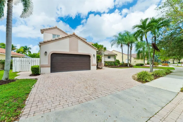 Stucco exterior featuring a dual-tone facade, attached two-car garage, and a decorative paver driveway