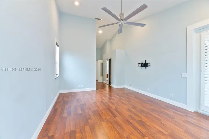 Vaulted ceilings featuring recessed lighting, a brushed-metal ceiling fan, wood-finish flooring, and a glass-paneled exterior door with shutters