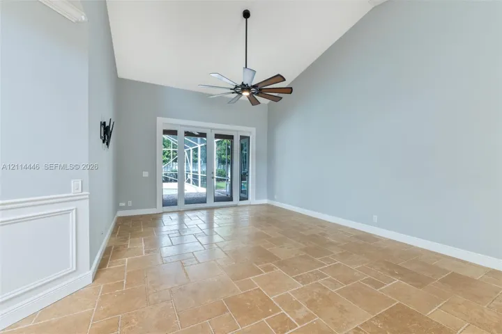 Vaulted ceilings featuring a multi-blade ceiling fan, stone-tile flooring, and glass-paneled exterior doors with an integrated screen​​‌​​​​‌​​‌‌​‌‌​​​‌‌​‌​‌​‌​​​‌​​ enclosure