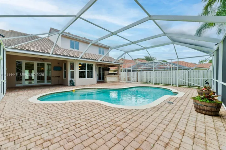 Screen-enclosed patio with paver decking, freeform swimming pool, built-in outdoor kitchen, and tile roof