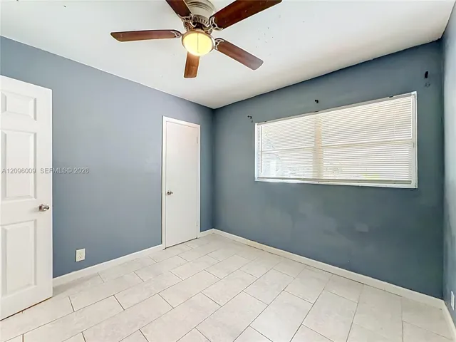 Room featuring tile flooring, a central ceiling fan with an integrated light fixture, two panel-style doors, and a horizontal window with adjustable blinds