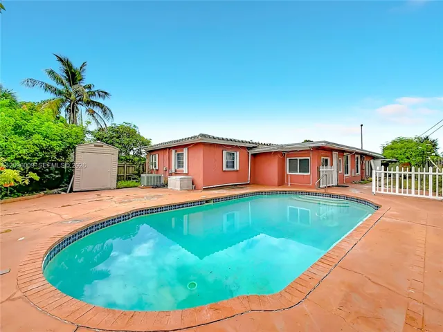 In-ground swimming pool with tile trim, expansive concrete patio, stucco exterior finish, and detached outdoor storage structure