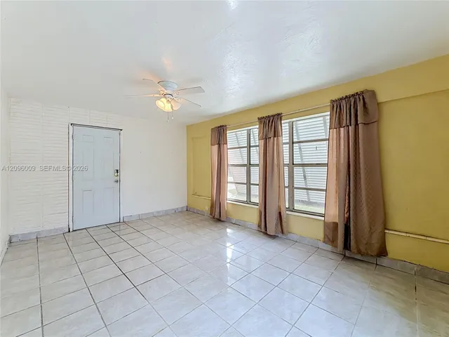 Interior space featuring ceramic tile flooring, a painted brick accent wall, and a central ceiling fan with integrated lighting