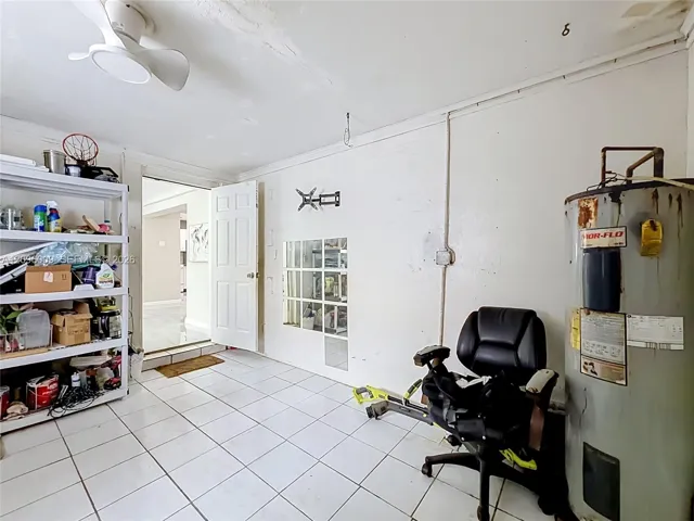 Utility room featuring tile flooring, a wall-mounted ceiling fan with integrated lighting, a glass-block accent panel, and a six-panel interior door