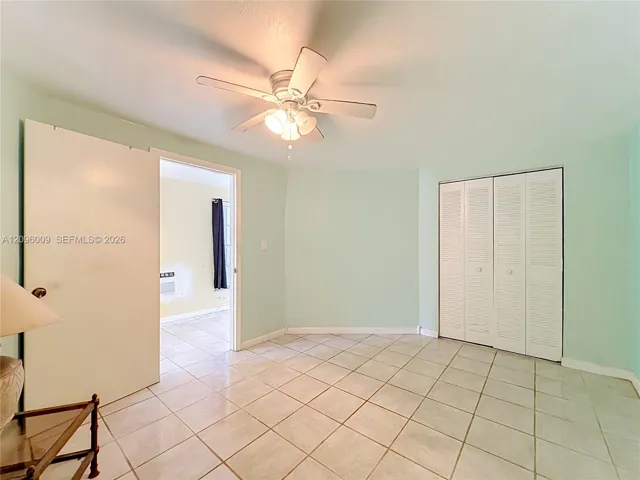 Tile flooring, light-toned wall paint, white louvered-door closet, and ceiling fan with integrated lighting