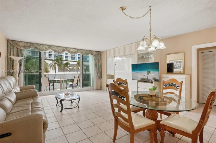 Living area featuring large-format ceramic tile flooring, floor-to-ceiling glass sliding doors, built-in cabinetry with overhead storage, and a multi-arm brass chandelier