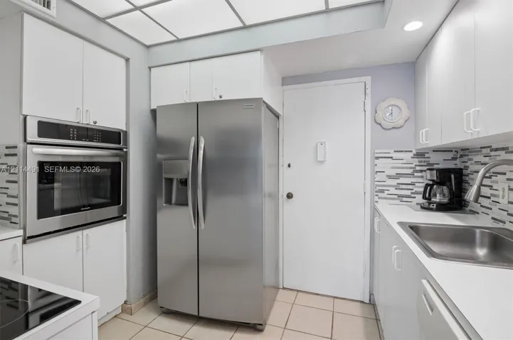 Kitchen featuring white cabinetry, stainless steel side-by-side refrigerator, built-in stainless steel wall oven, tile backsplash, and recessed lighting