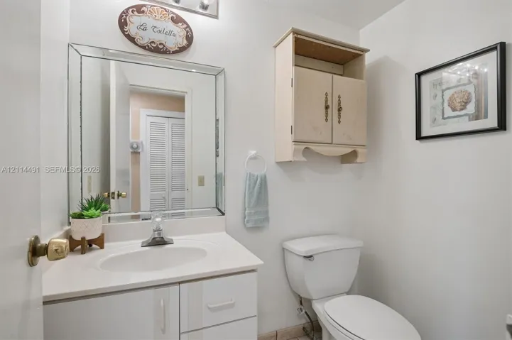 Bathroom featuring a white vanity cabinet with a stone-finish countertop, an oval undermount sink, a beveled-edge wall mirror, and a wall-mounted wooden storage cabinet
