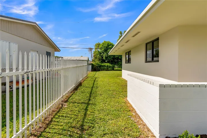 Exterior side yard featuring a white picket-style fence, manicured grass, low-profile concrete masonry wall, and roof overhang