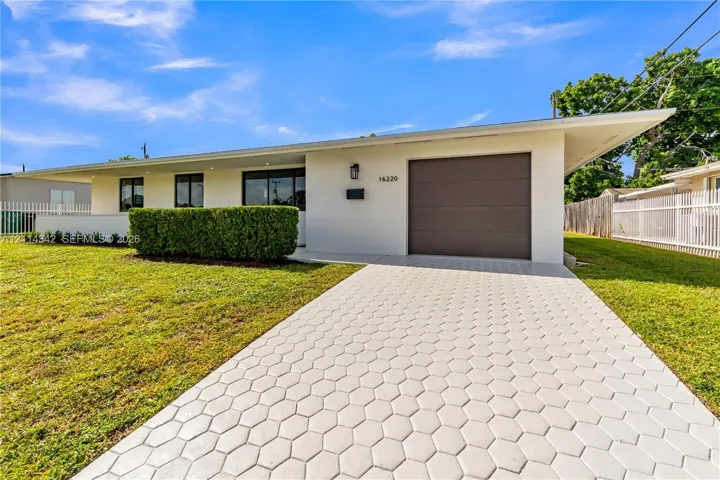 Mid-century modern exterior featuring painted brick facade, overhanging eaves, an integrated one-car garage, and a geometric hexagonal paver driveway