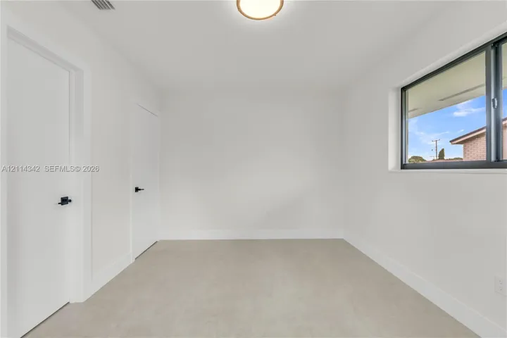 Bright interior featuring neutral-toned flooring, two doors with matte black hardware, a flush-mount ceiling light, and a window with a dark frame