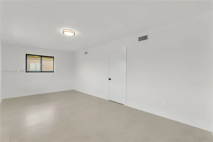Neutral interior space featuring light-toned flooring, a single window with a black frame, and a circular flush-mount ceiling light fixture