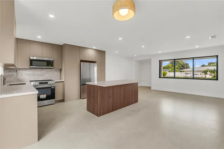 Kitchen featuring flat-panel cabinetry, a wood-finish island, solid-surface countertops, stainless steel appliances, and tile flooring