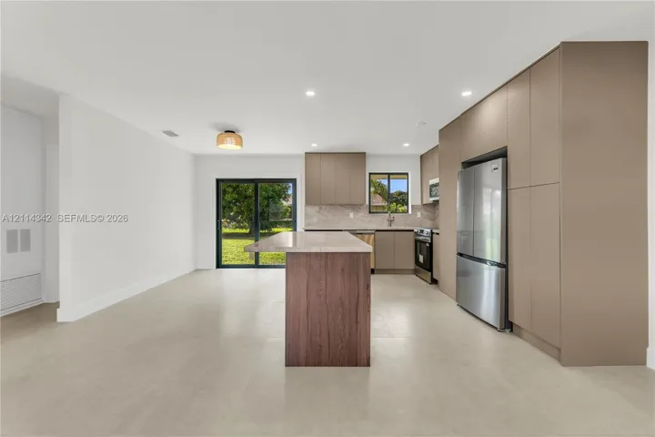 Kitchen featuring flat-panel cabinetry, a wood-finish central island with a stone-top breakfast bar, stainless steel appliances, and large-format tile flooring