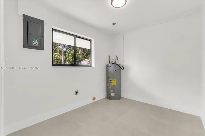 Utility space featuring neutral-toned tile flooring, a mounted electrical panel, a sliding window, and a vertical water heater