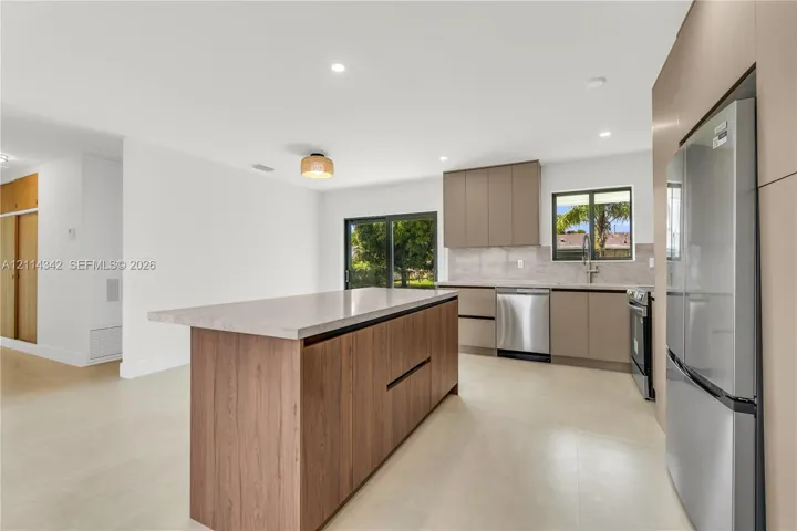 Kitchen featuring a wood-finish island, solid-surface countertops, flat-panel cabinetry, stainless steel appliances, and recessed lighting