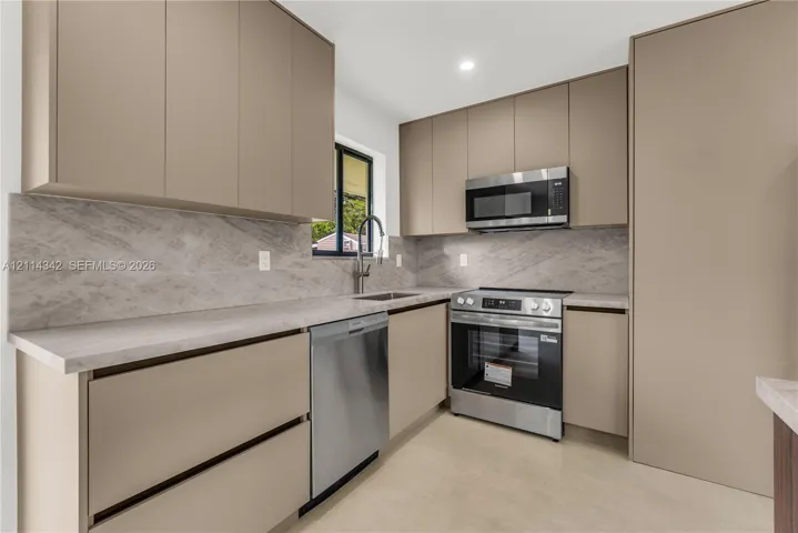 Modern kitchen featuring flat-panel cabinetry, full-height stone-patterned backsplash, light-toned countertops, and stainless steel appliances